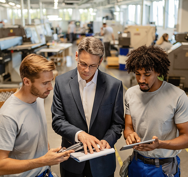 Skilled worker staffing two steel workers going through quality reports while working in industrial building.
